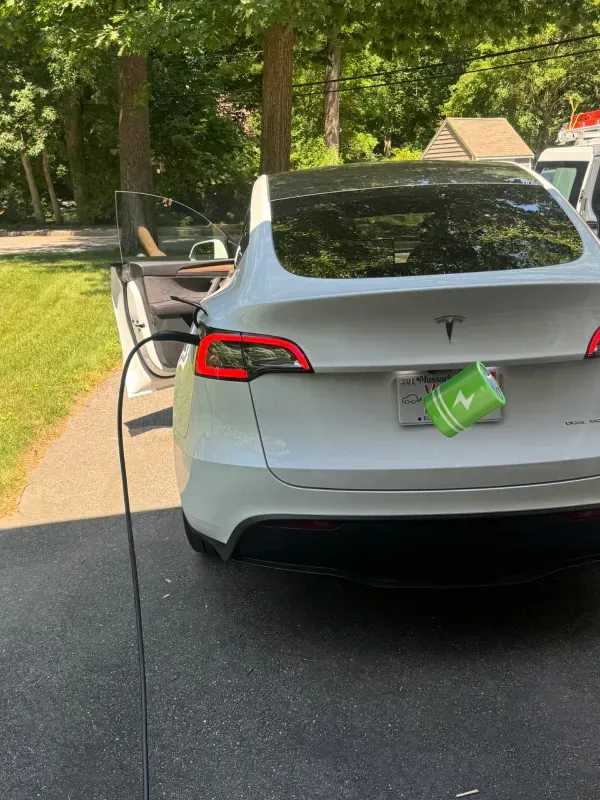 A white tesla model 3 is being charged in a driveway.