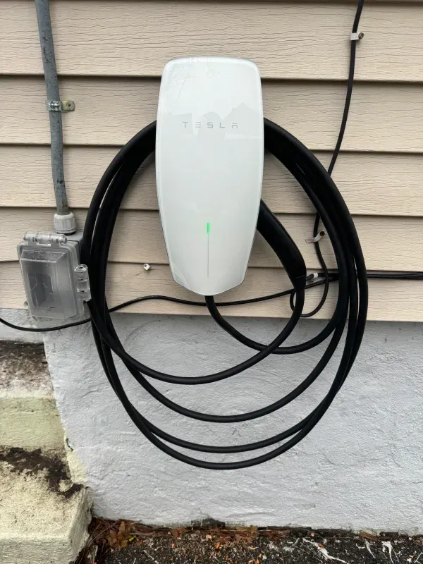 A tesla charging station is attached to the side of a house.