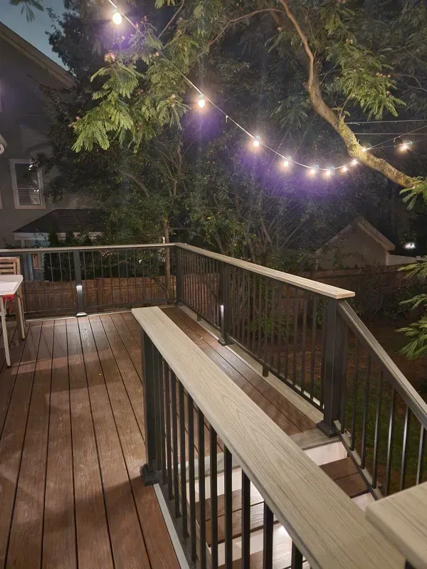 A wooden deck with a railing and lights on it at night.