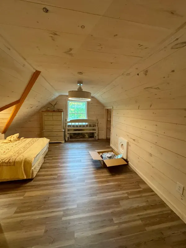 A bedroom in an attic with a bed , dresser , and bunk bed.