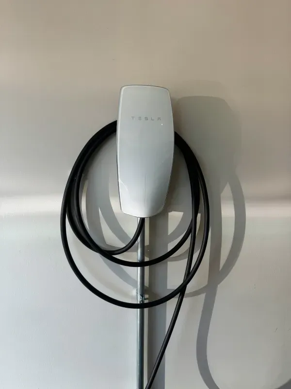 A white tesla charging station with a black cable attached to it