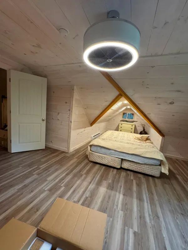 There is a bed in the attic with a fan hanging from the ceiling.