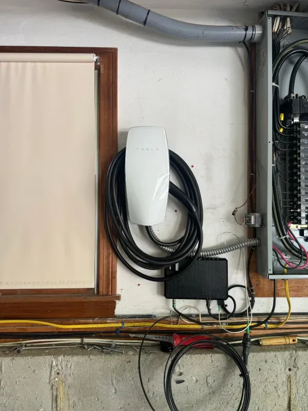 A tesla charging station is hanging on a wall next to a window.