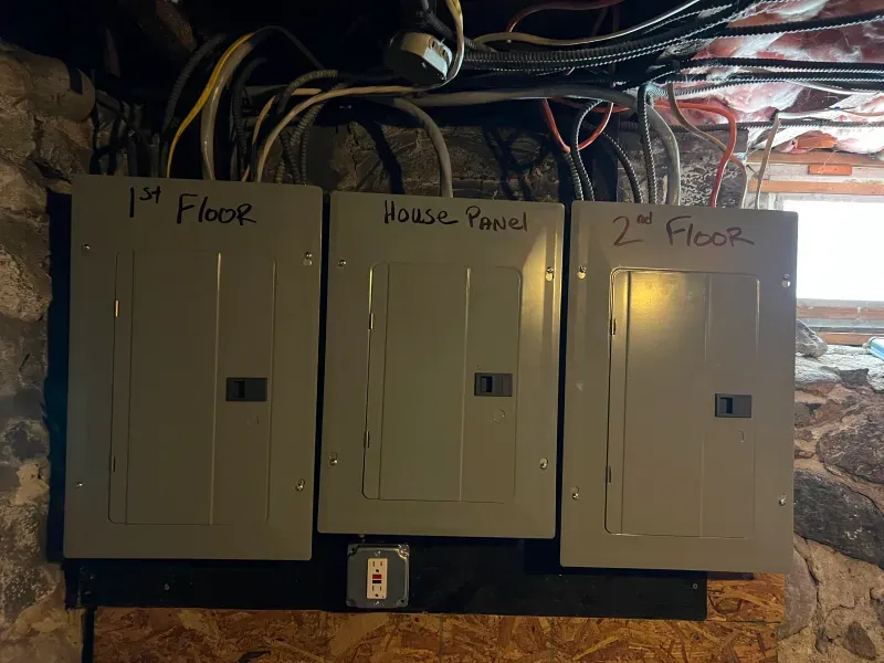 Three electrical panels are hanging on a wall in a basement.