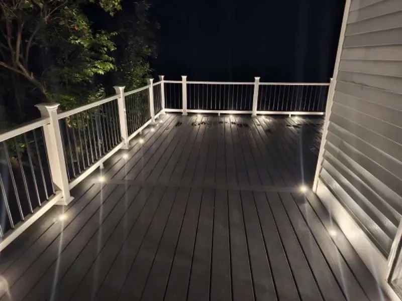 A deck with a white railing and lights at night