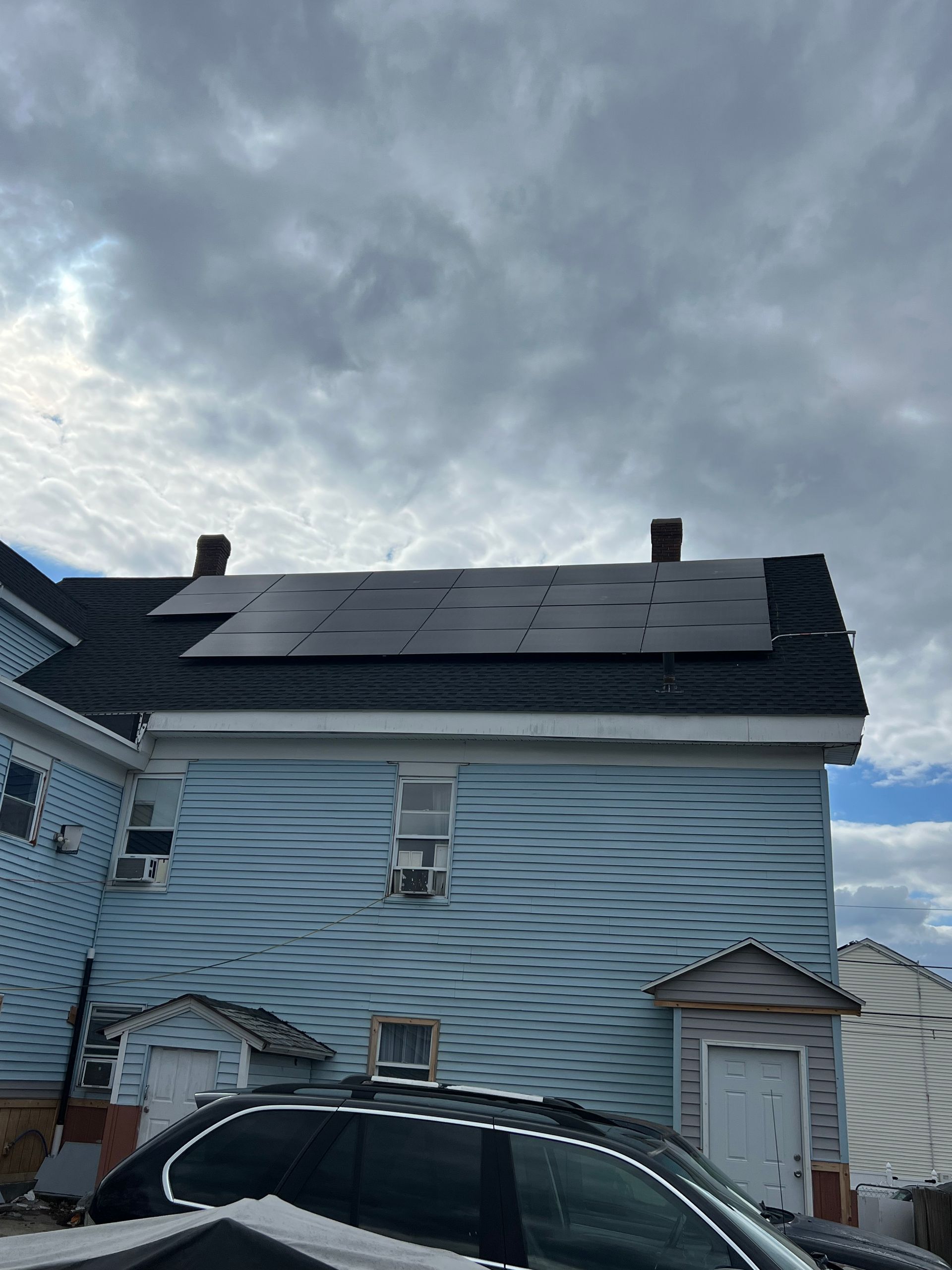 A blue house with solar panels on the roof and a car parked in front of it.