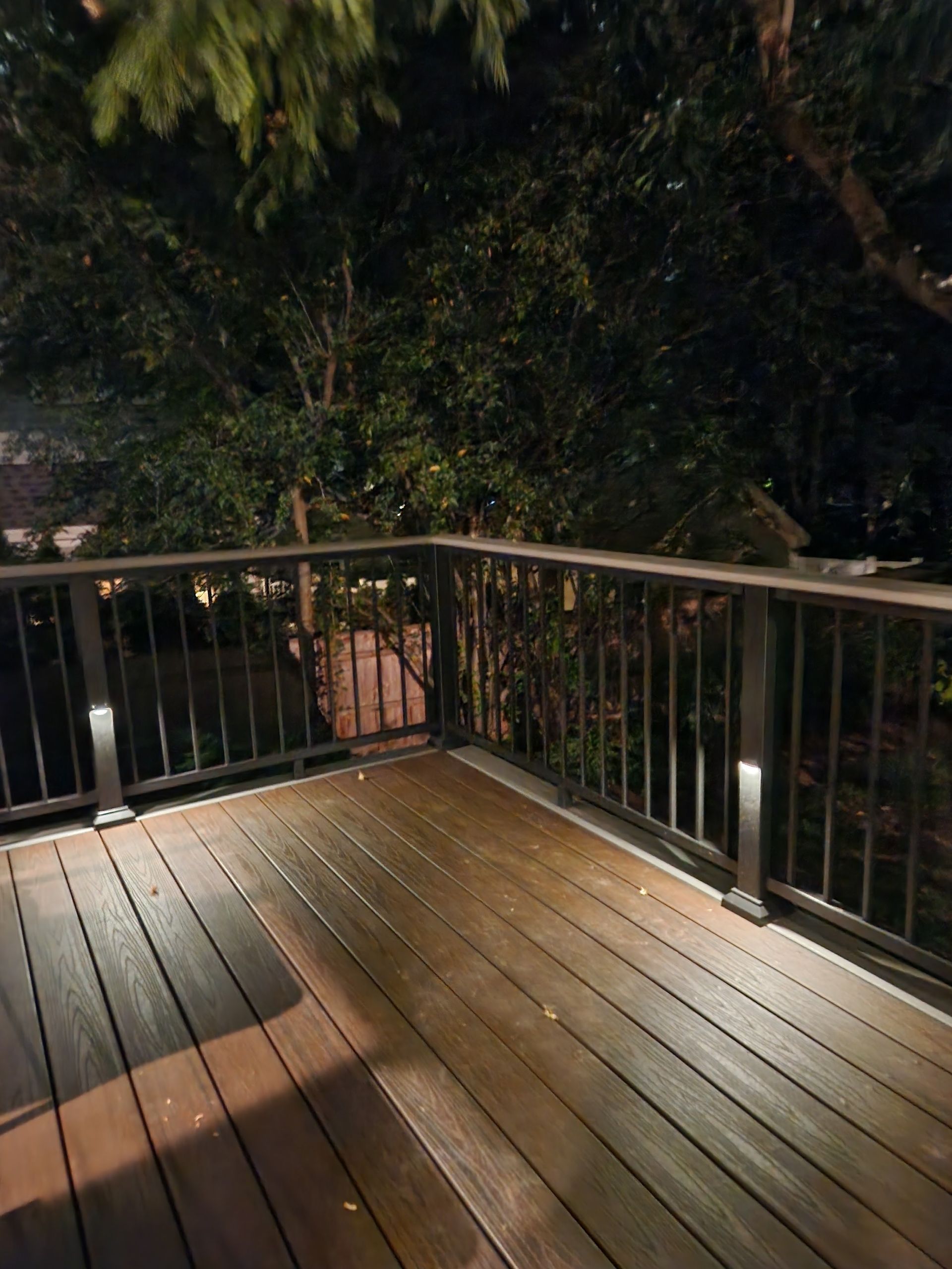 A wooden deck with a railing and lights at night.