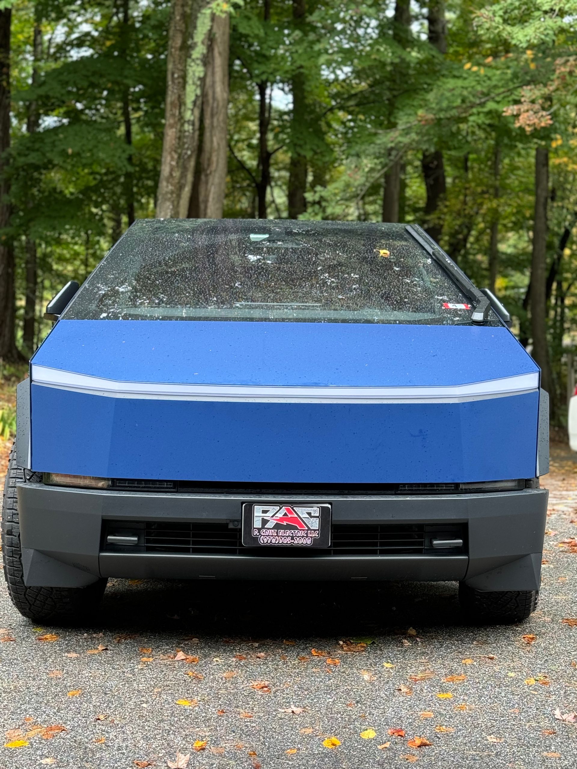 A blue car is parked in a gravel lot in the woods.