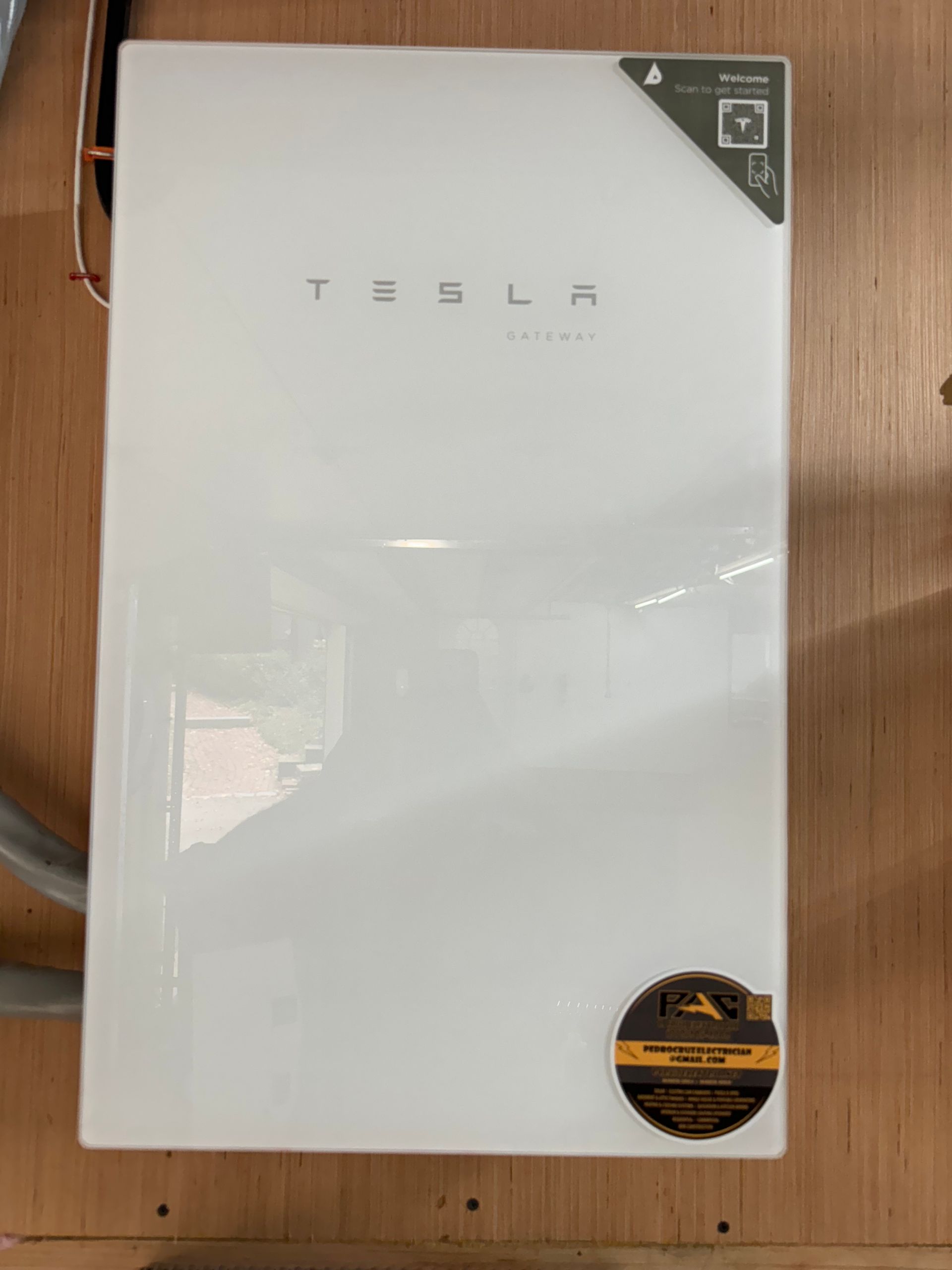 A white tesla battery is sitting on a wooden wall.
