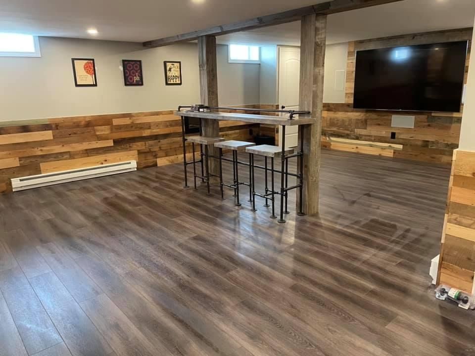 A basement with hardwood floors , stools , a table and a flat screen tv.