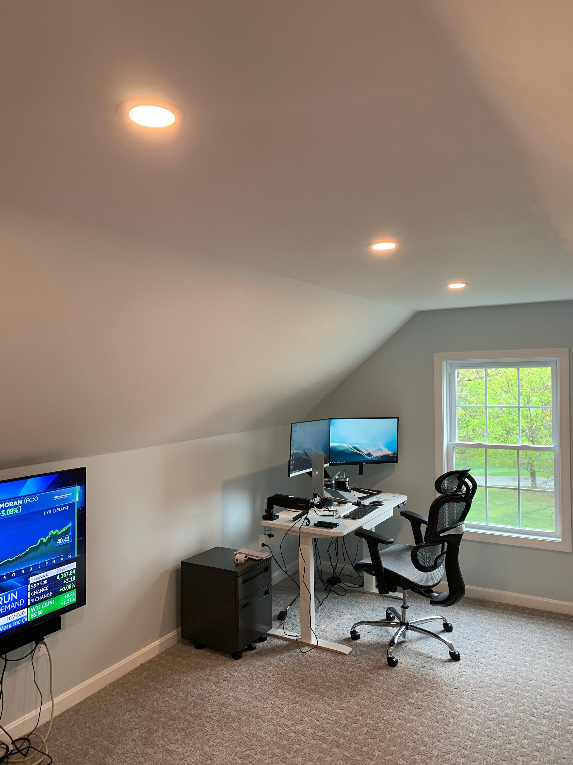 A room with a desk , chair , computer and television.