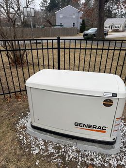 A generator is sitting in the grass next to a fence.