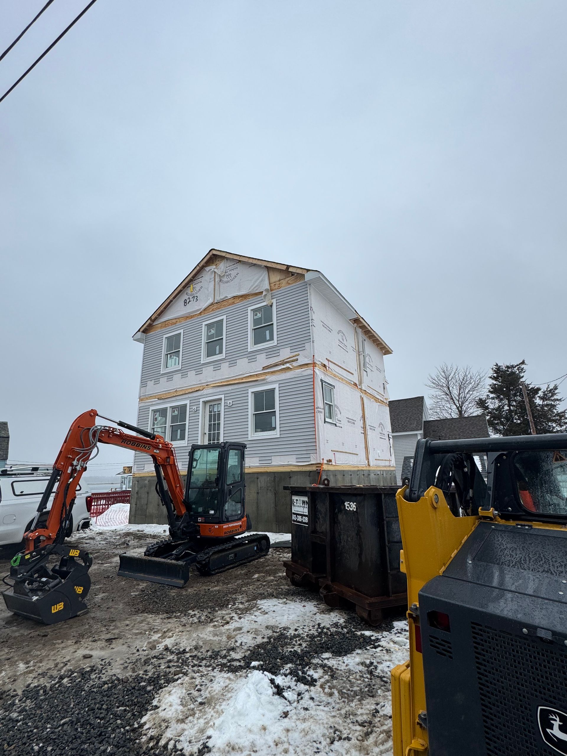A house is being built in the snow with an excavator in front of it.