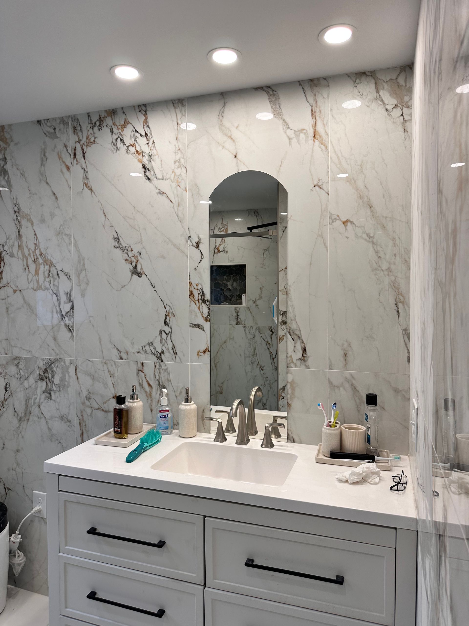 A bathroom with a sink , mirror and marble walls.