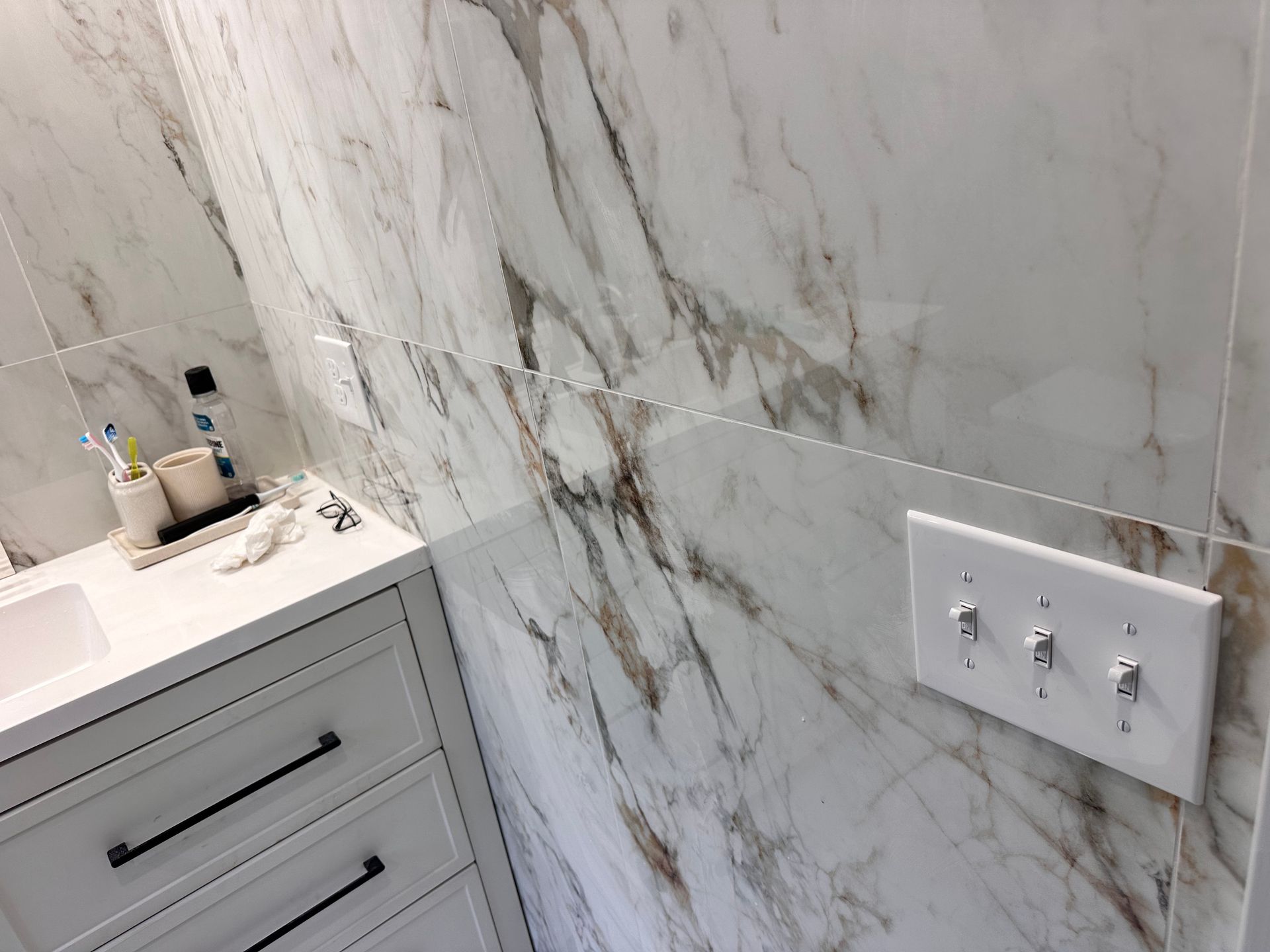 A bathroom with marble tiles , a sink , and a light switch.