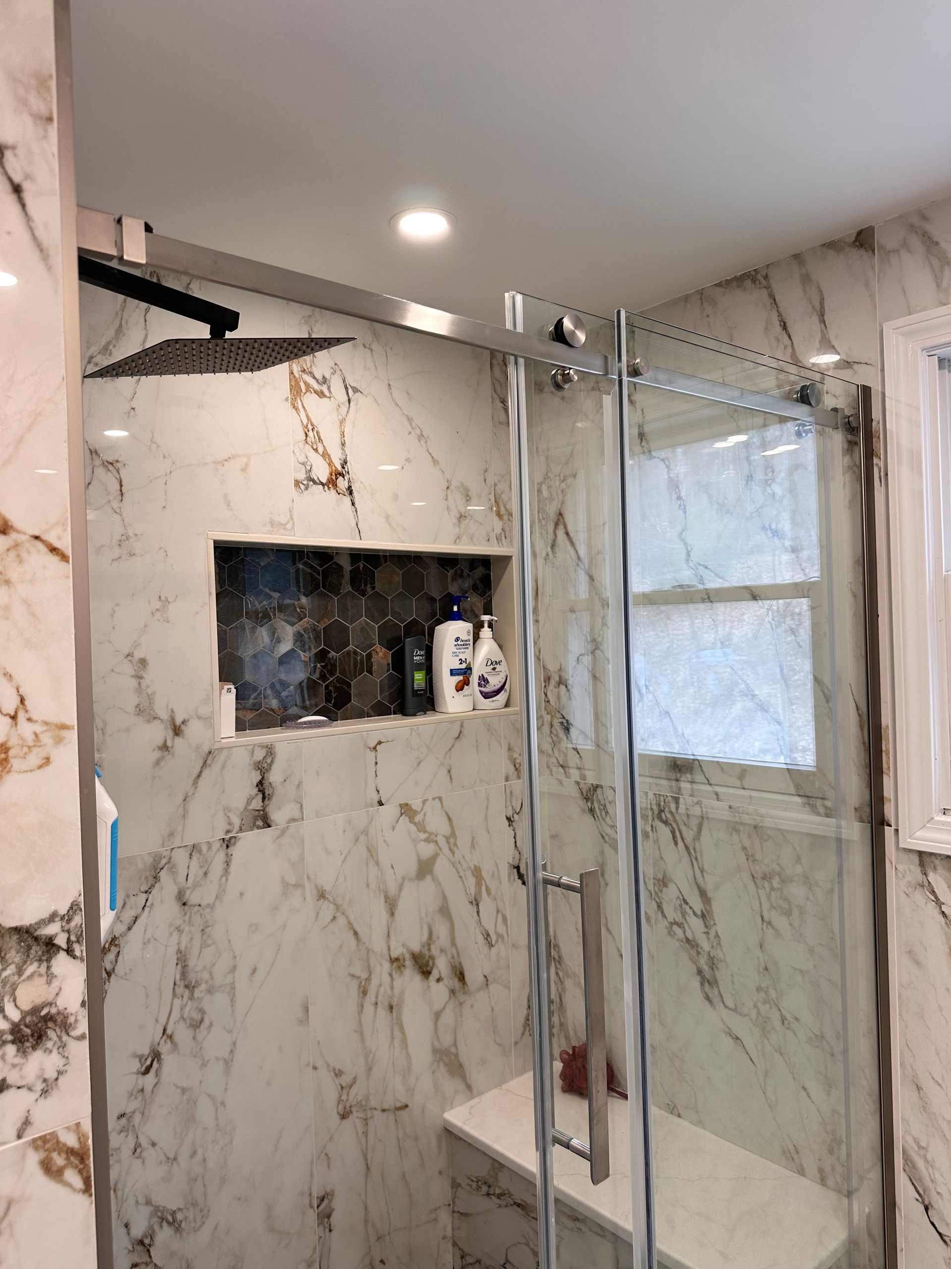A bathroom with marble walls and a sliding glass shower door.