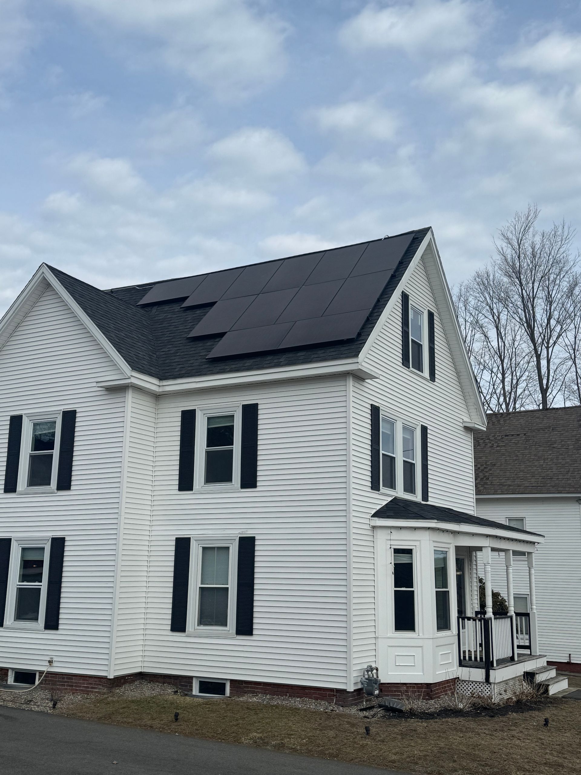A white house with black shutters and solar panels on the roof.