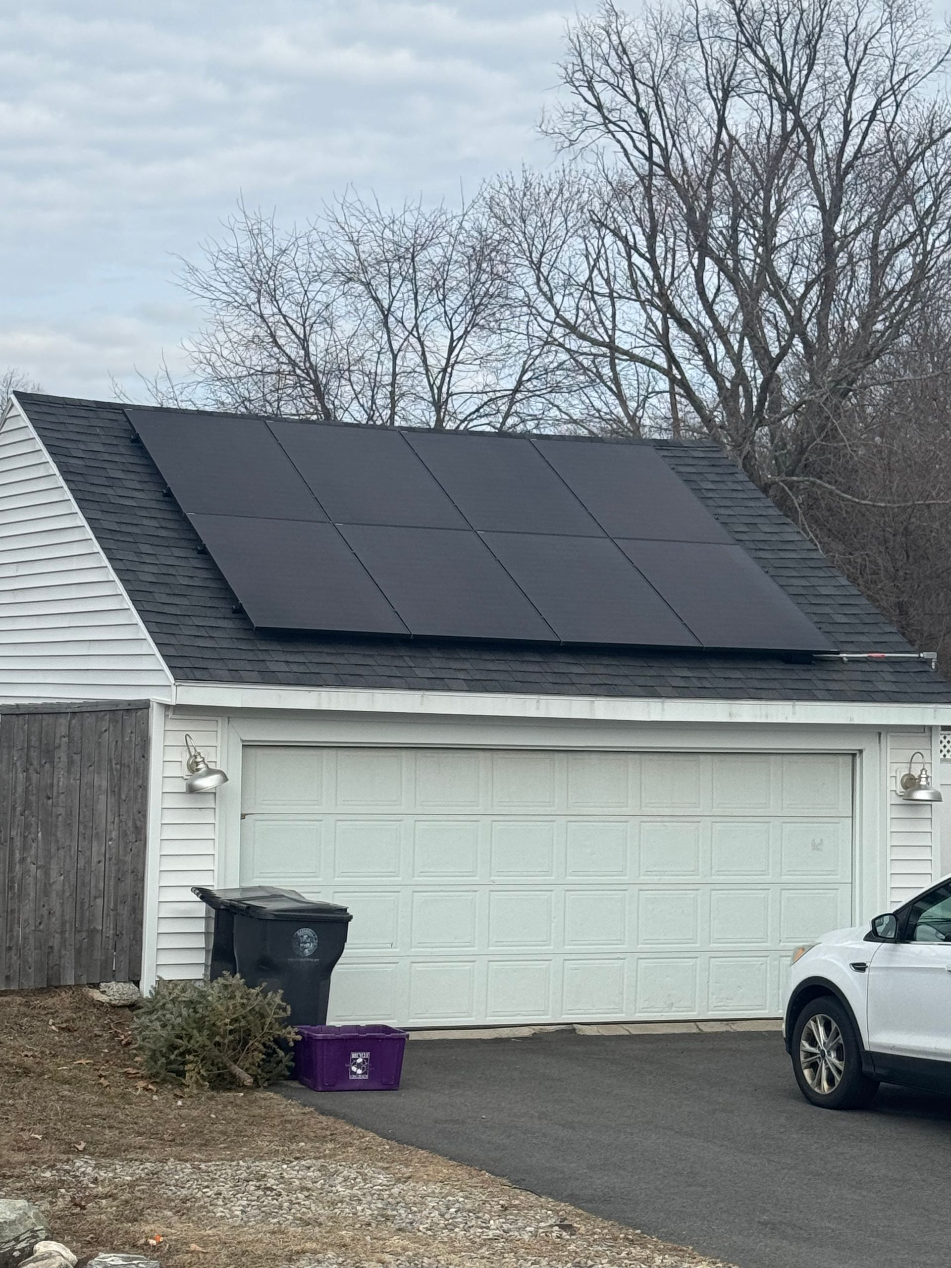 A car is parked in front of a garage with solar panels on the roof.