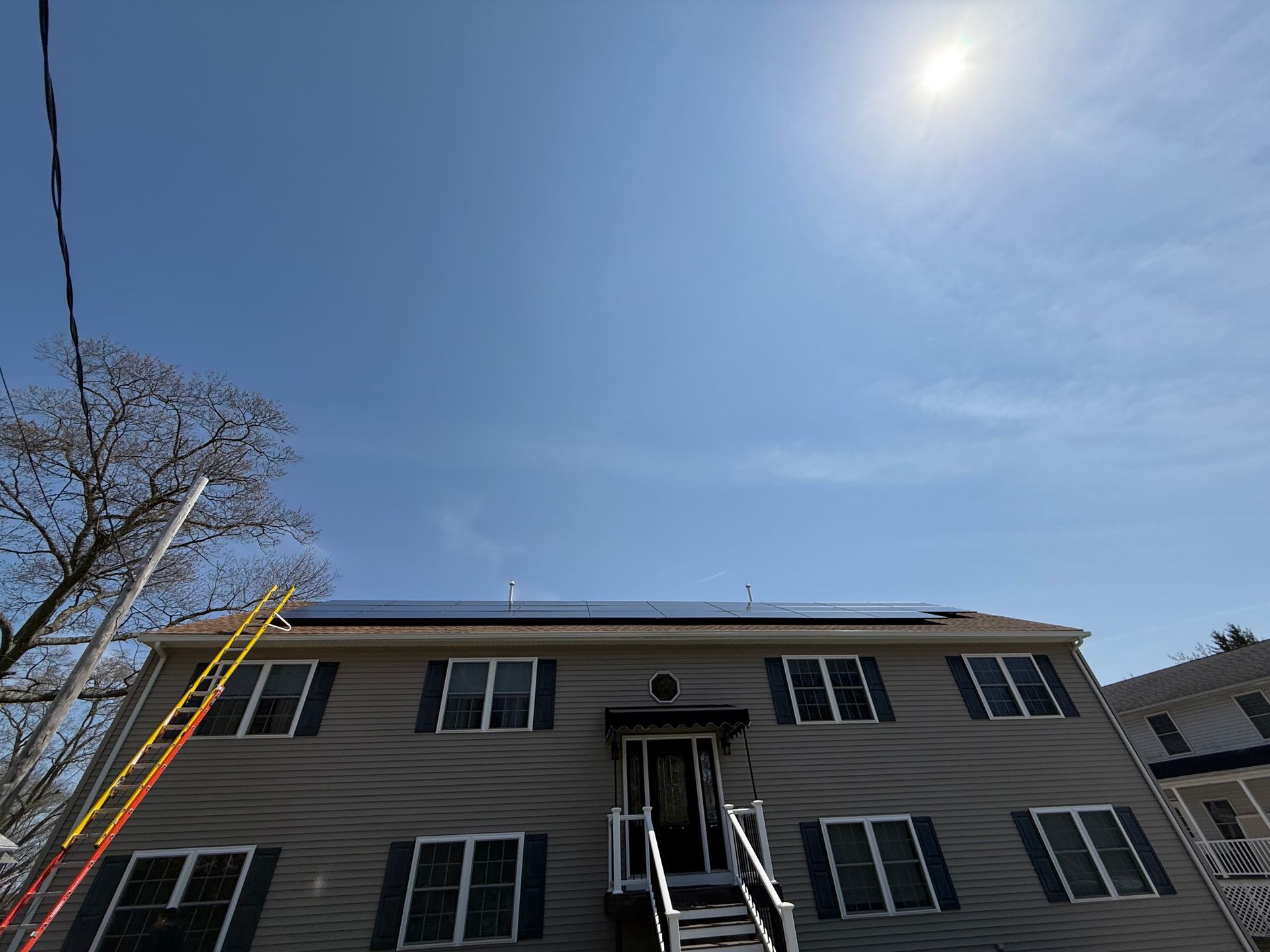 A house with solar panels on the roof and a ladder in front of it.