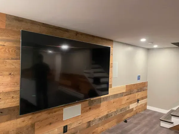 A flat screen tv is hanging on a wooden wall in a living room.