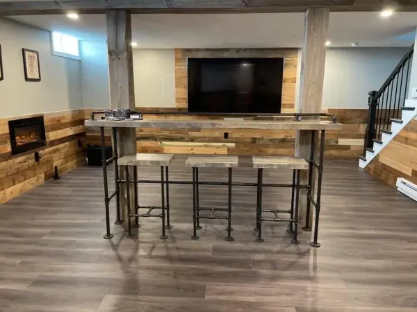 A basement with a bar and stools and a flat screen tv.