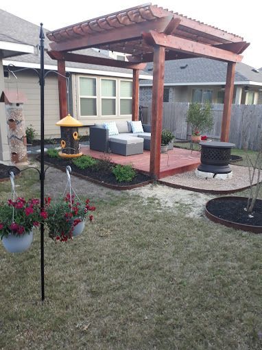 There is a pergola in the backyard with a couch and a bird feeder.
