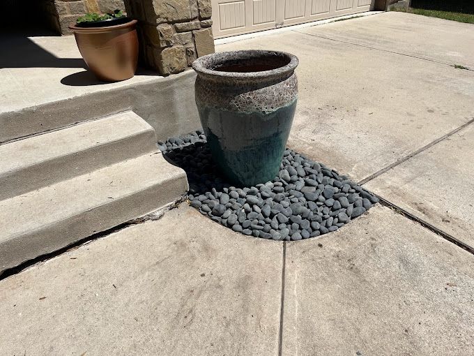 A blue vase is sitting on a concrete sidewalk next to stairs.