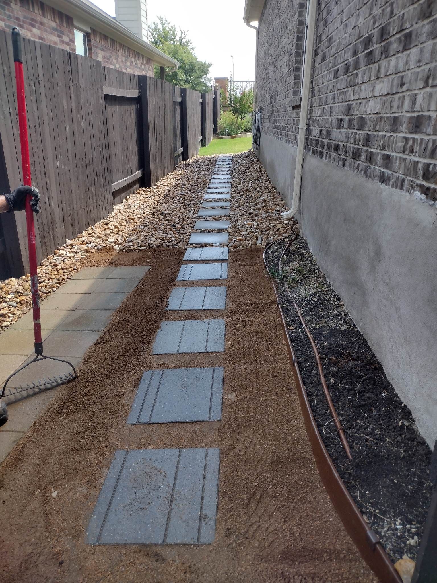 Stone path with gravel and brick wall next to wooden fence.