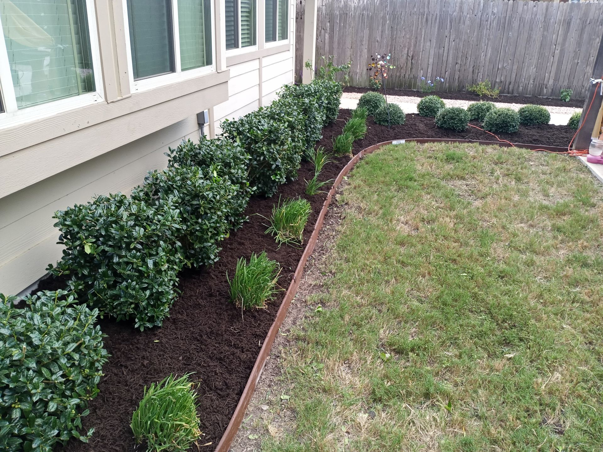 A neatly landscaped yard with green bushes and fresh mulch. Grass is on the right side.