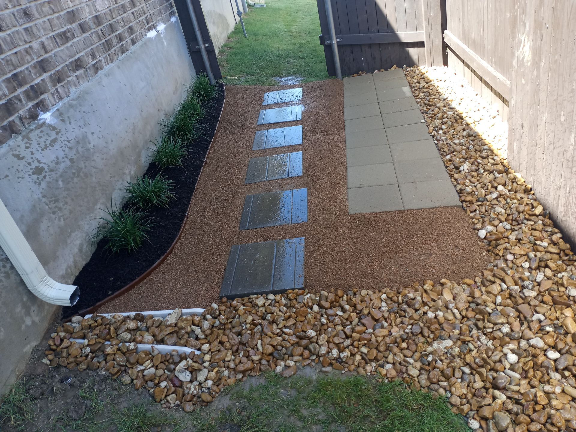 Stone pathway with landscaping between a brick wall and wooden fence.