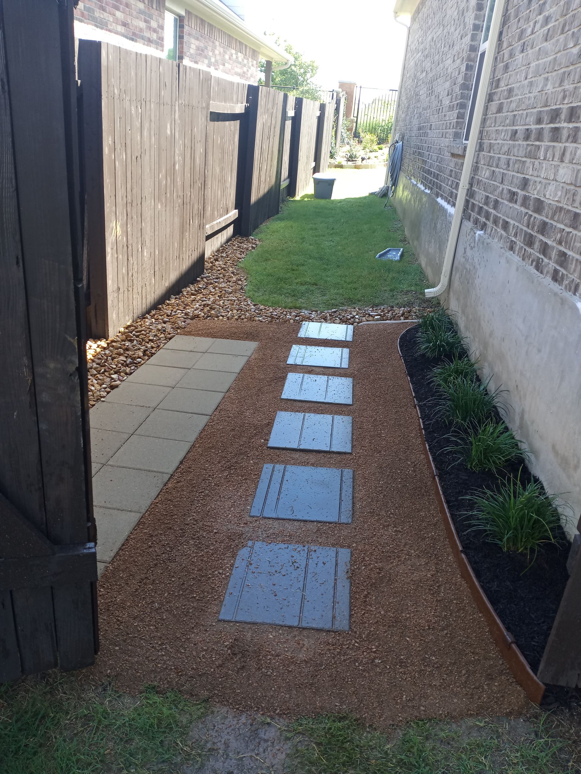 Stone path leading through a narrow side yard between a wooden fence and a brick wall.