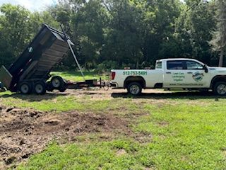 A white truck with a dump trailer attached to it is parked in a grassy field.