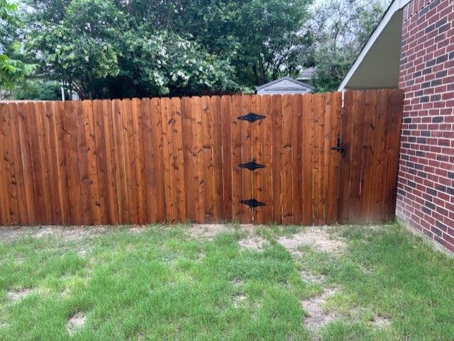 A wooden fence with a gate in the backyard of a brick house.