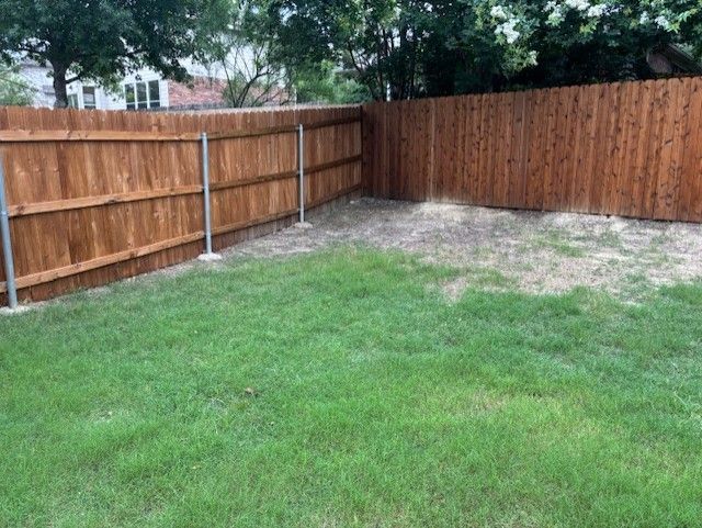 A backyard with a wooden fence and a lush green lawn.