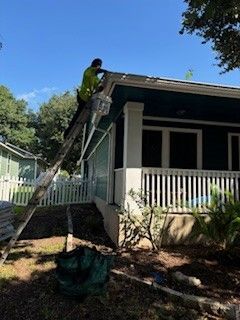 A man is painting the roof of a house with a ladder.