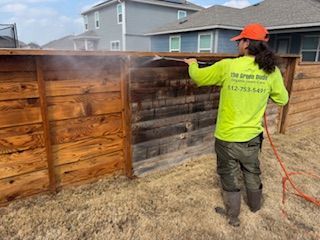 A man in a yellow jacket is cleaning a house with a high pressure washer.