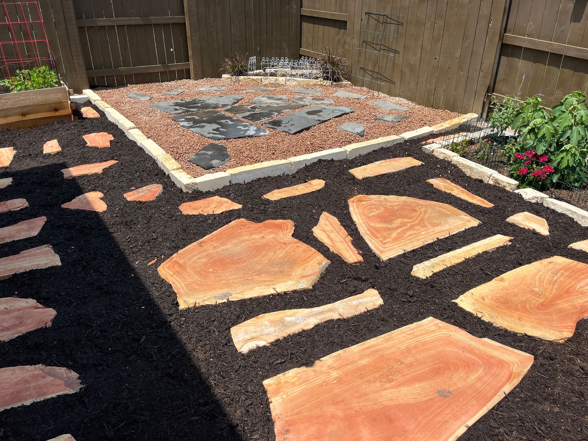 A stone walkway in a backyard with a fence in the background.
