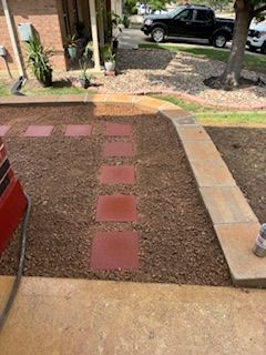 Path with red pavers and brown gravel leading to a front door, with a sidewalk along side.