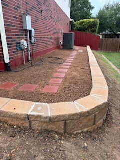 Curved retaining wall with a pathway of red pavers, next to a red brick building.