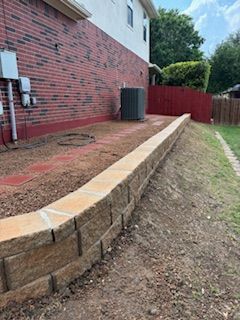 Brick house with a stone retaining wall. The yard slopes downwards.