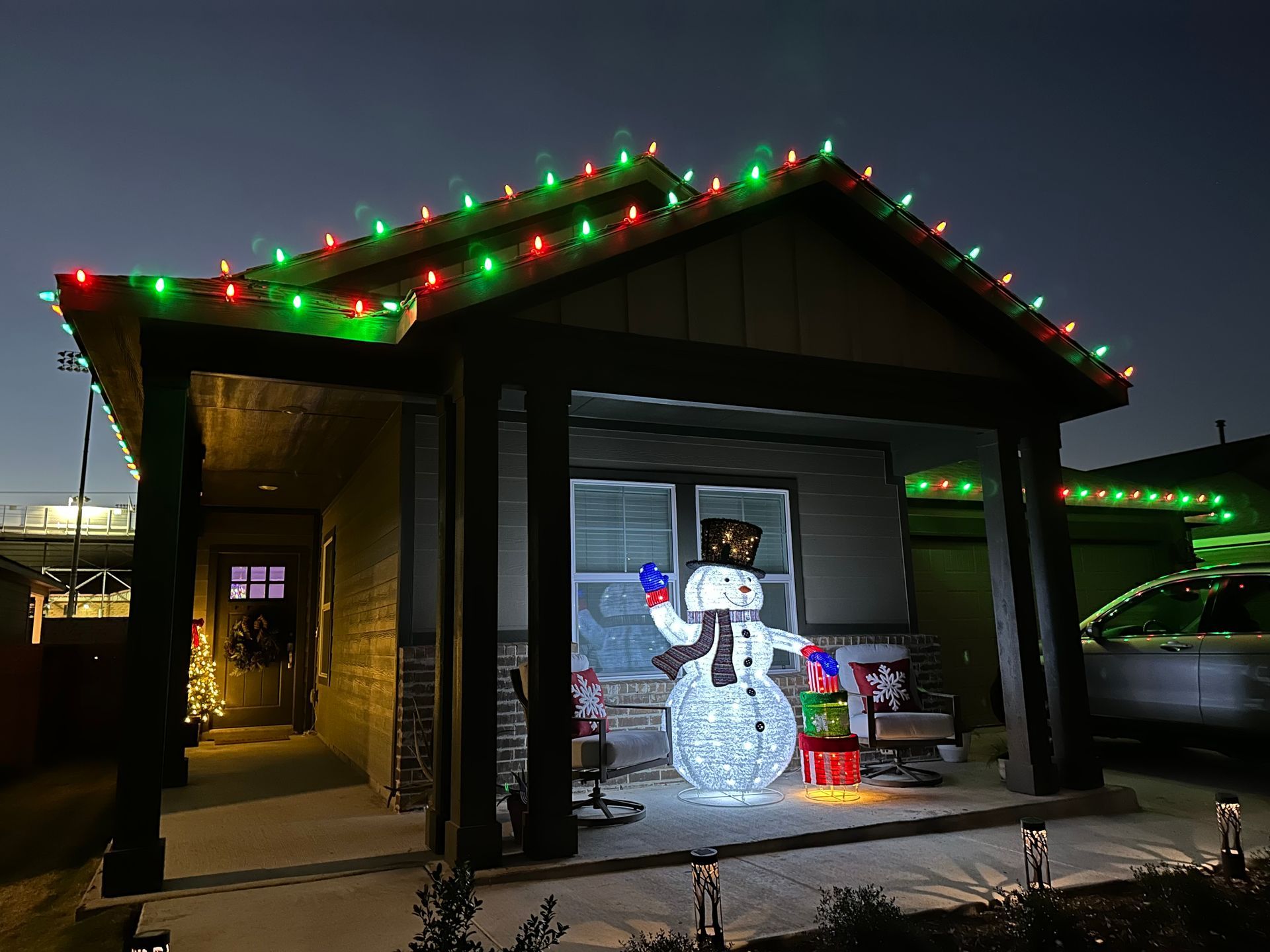 A house with christmas lights and a snowman in front of it.