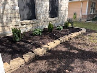 A landscaped garden bed with a stone border in front of a light-colored brick house.