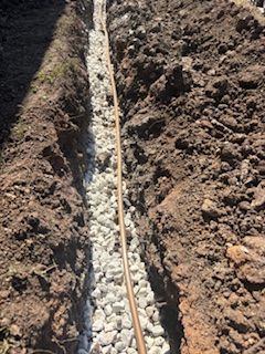 A trench filled with gravel and a brown pipe, dug in dirt.