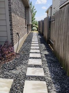 Stone path between a brick building and a wooden fence, surrounded by gravel.