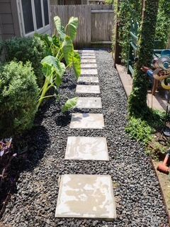 Stone path through a garden with gravel, bordered by plants and a wooden fence.
