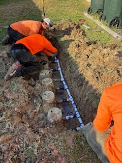 Three people in orange shirts install an irrigation system in a trench.