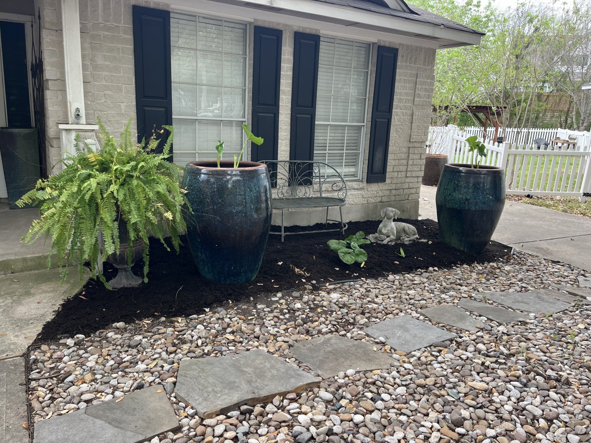 A stone walkway leading to a house with potted plants in front of it.