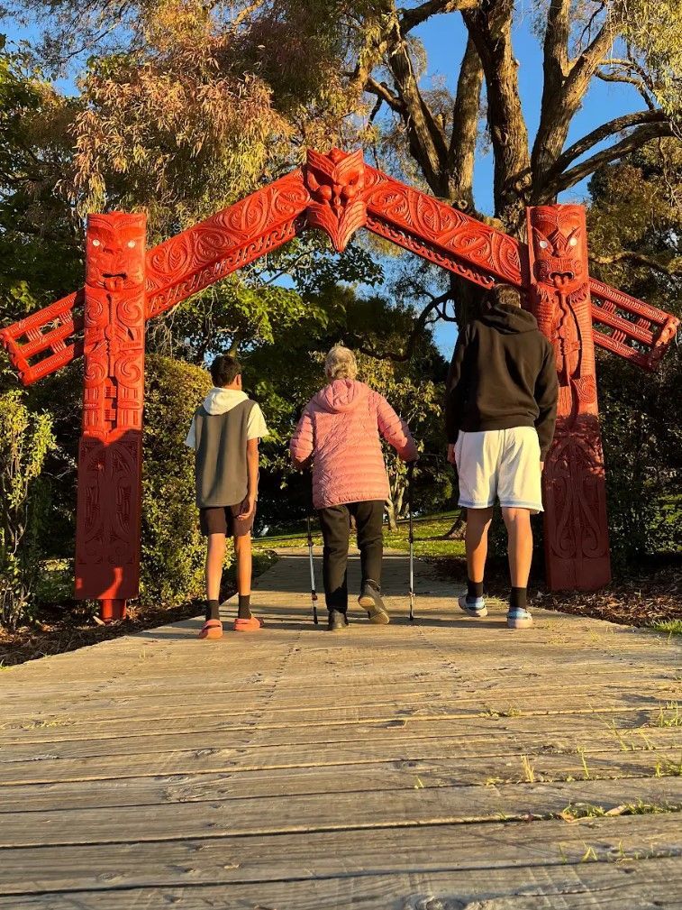 A group of people are walking under a red archway in a park.