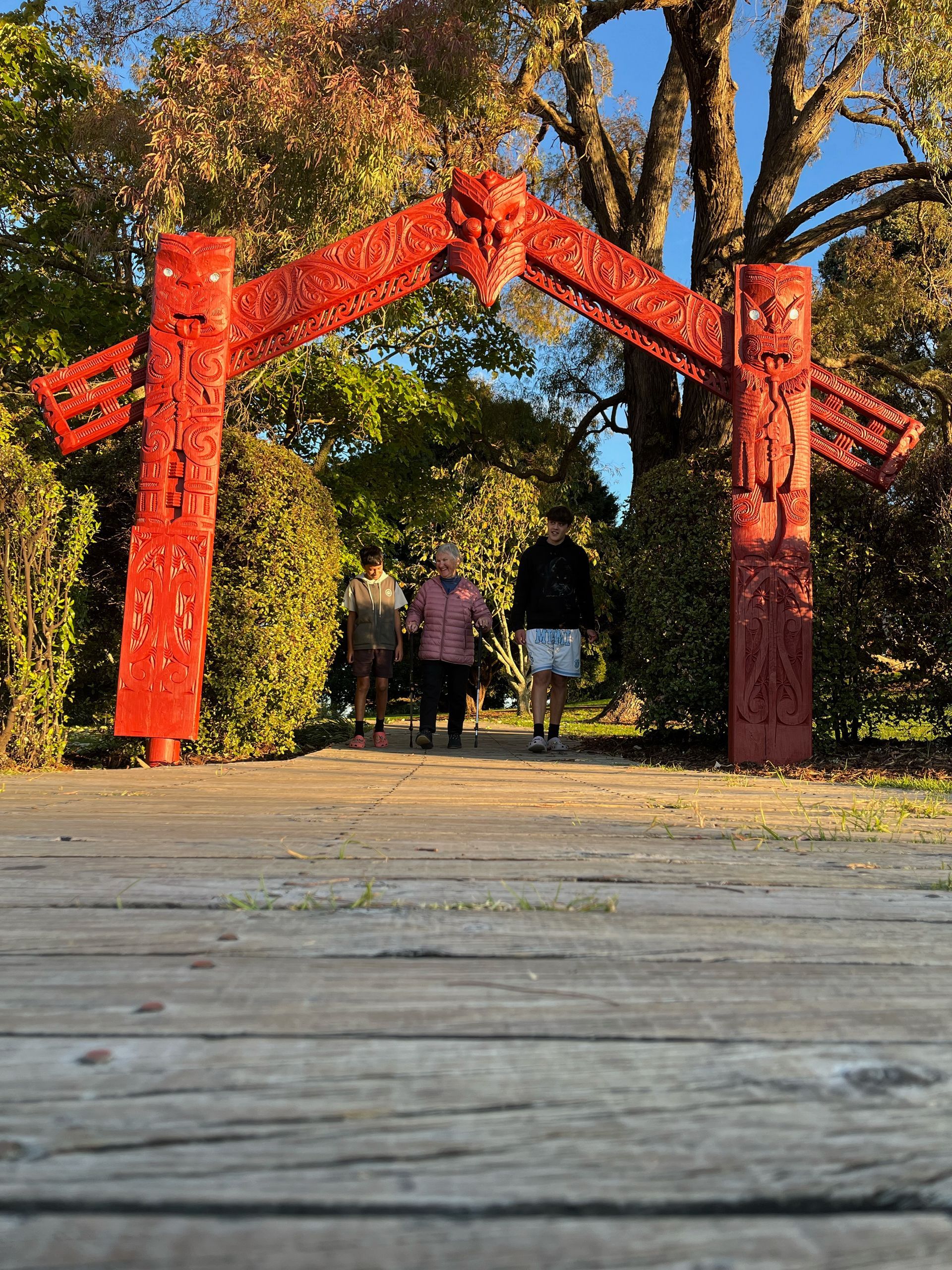 A couple of people walking under a red archway in a park.