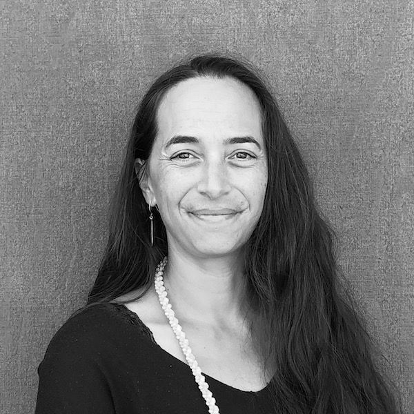 A woman with long hair and a pearl necklace is smiling in a black and white photo.